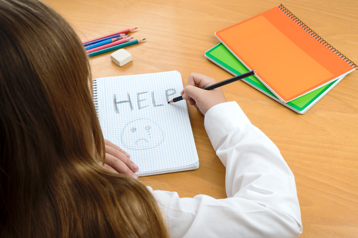 A Horizontal image /poster covering the Social Issues of child abuse, by a schoolchild sat at a desk asking for help by a written message saying Help with a sad face . Room for copy space and text